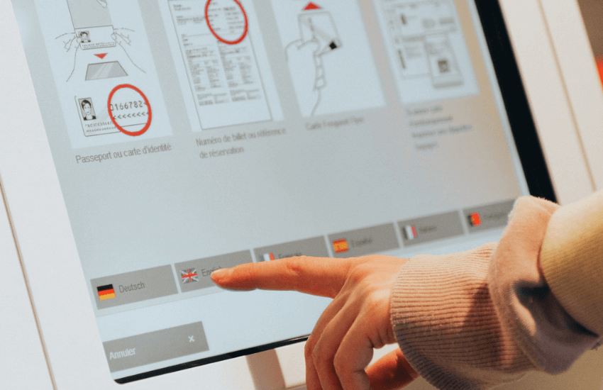Eine Person berührt einen Touchscreen, um eine Sprache aus einer Reihe von Flaggen auszuwählen (Deutsch, Englisch usw.).