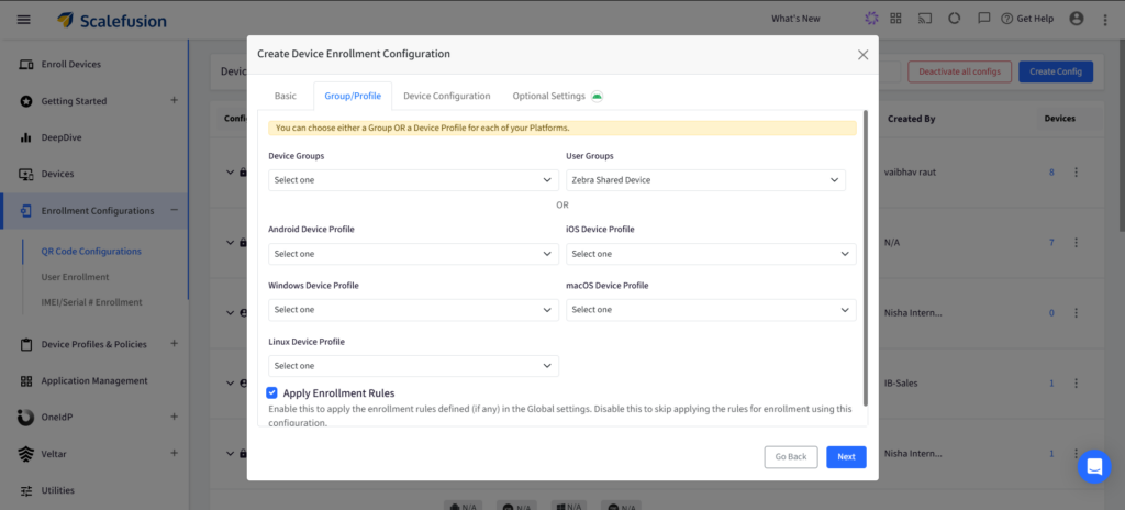Cuadro de diálogo titulado "Crear configuración de inscripción de dispositivos" con pestañas para Básico, Grupo/Perfil, Configuración del dispositivo y Ajustes opcionales; campos de formulario para elegir Grupos de dispositivos, Grupos de usuarios y perfiles por plataforma; incluye una casilla de verificación "Aplicar reglas de inscripción" y botones de navegación (Volver, Siguiente).